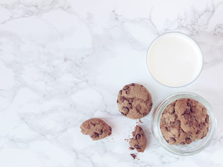 Crisp chocolate cookies with a glass of milk on marble background. Flat lay. Top view
