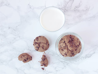 Crisp chocolate cookies with a glass of milk on marble background. Flat lay. Top view