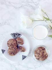 Crisp chocolate cookies with a glass of milk and white flower on marble background. Flat lay. Top view