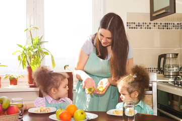 Obraz na płótnie Canvas Family preparing meal together. Happy mother and her cute twin daughters having fun cooking fruit salad.