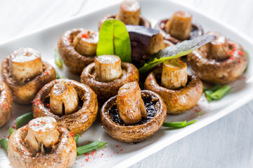 Grilled champignon white mushrooms on white plate with herbs and spices. Close up with selective...