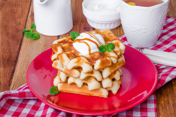 Stack Belgian waffles with caramel sauce and whipped cream on a plate.