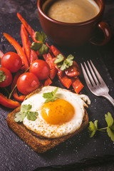 Fried egg on toast  with vegetables and coffee on dark stone background