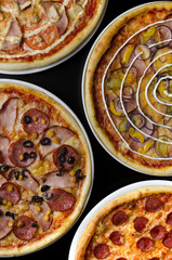 Four different pizzas on a white plate and a black table