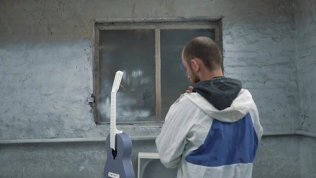 Painter looks at the guitar and smokes. And the light goes out in the spray booth