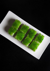 Green sushi on white plate on a black background