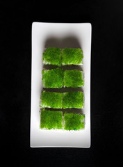Green sushi on white plate on a black background