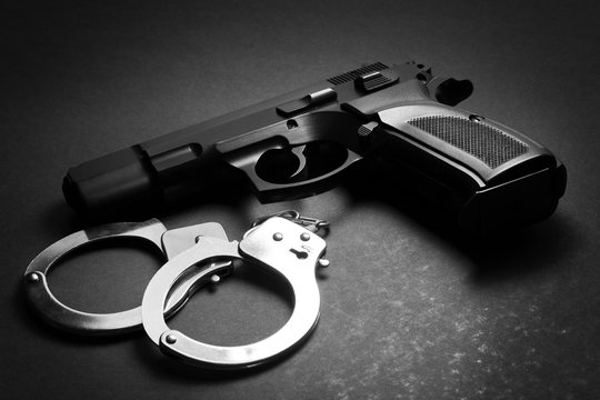 handgun with handcuffs on dark background, crime concept, law enforcement