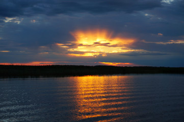 Sunset over the water. The sun makes its way through the clouds.