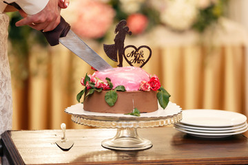 chocolate wedding cake for the newlywed decorated in the red flowers and heart. A figure of the groom and bride on a pie.