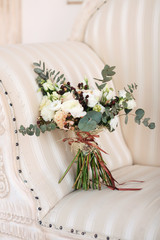 Bridal bouquet. The bride's bouquet. Beautiful bouquet of white, and beige flowers and greenery, decorated with long silk brown ribbon lies on a on a beige vintage sofa