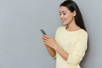 Happy attractive young woman standing and using mobile phone