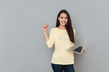 Smiling beautiful young woman holding laptop and pointing away