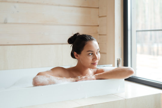 Smiling woman sitting and looking at the window in bathtub