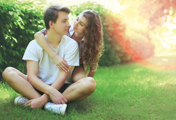 Happy sweet young couple teenagers sitting on the grass in summer day