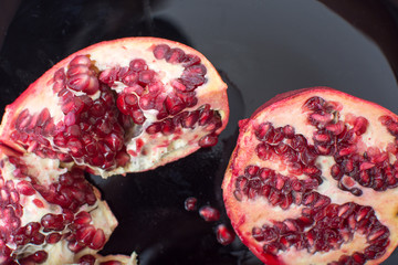 Broken red ripe pomegranates in black plate.