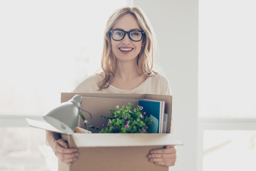 Concept of promotion at work. Young dreaming pretty smiling woman in glasses holding her belongings in cardboard box