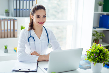 Horizontal photo of young smiling therapist sitting at the table at her medical office