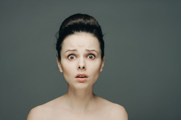 surprised woman with wide eyes and bare shoulders on a gray background