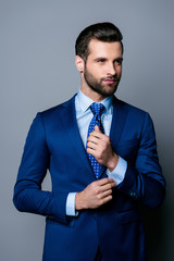 Portrait of serious fashionable handsome man posing in blue suit and tie  buttoning cufflinks