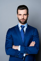 Portrait of serious fashionable handsome man in blue suit and tie  crossing hands and look at camera