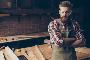 Bearded handsome joiner  think and look at camera near tabletop with tools.  Stylish young...