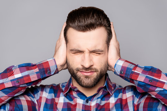 Frustrated handsome man covering his ears with hands standing against gray background