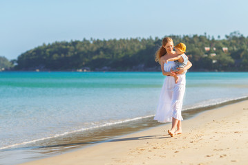 Fototapeta premium happy family mother with baby son walks by ocean on beach in summer