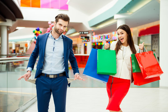 No more money for shopping. Man showing his empty pockets while his wife excited jump with shopping bags.