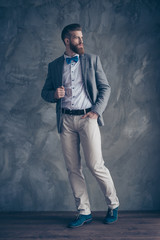 Full-length portrait of stylish hipster brutal young man with red mustache, beard and beautiful hairstyle ready for event party while standing on gray background