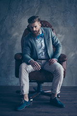 stylish serious minded brutal young man with red mustache, beard and beautiful hairstyle ponder while sitting on  comfortable office arm-chair and wearing formal clothes and trendy shoes