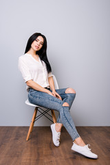 Young attractive calm woman posing on chair against gray background