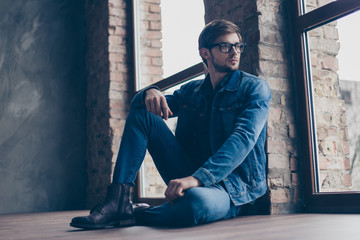 Confident cute smart man with spectacles in jeans sitting on the floor