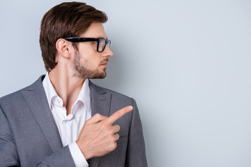 Side view portrait of young businessman in glasses and formalwear pointing on copyspace