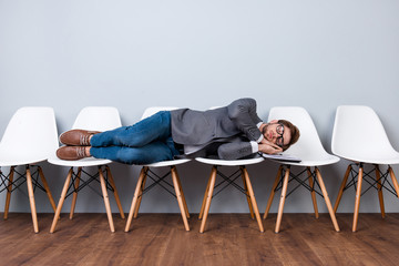 Young stylish man is sleeping on white chairs.