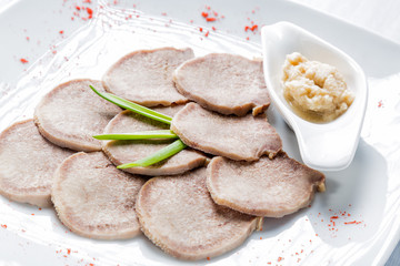 Boiled beef tongue with horseradish and herbs on white serving plate and wooden table. Selective focus