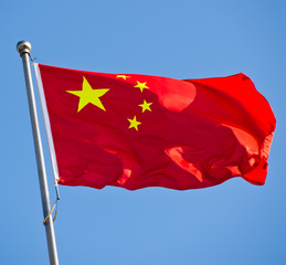 Chinese flag with flag pole waving in the wind over blue sky background.