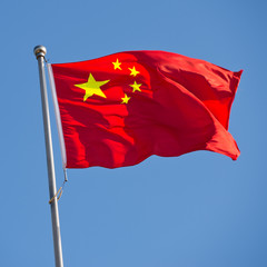 Chinese flag with flag pole waving in the wind over blue sky background.