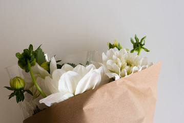 High angle view of white dahlias wrapped in clear cellophane and brown paper on white table