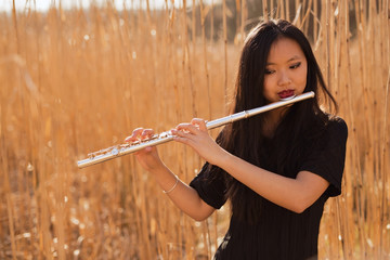 Beautiful Chinese, Oriental woman with long dark hair playing flute in a field of elephant grass © DavidOsborne