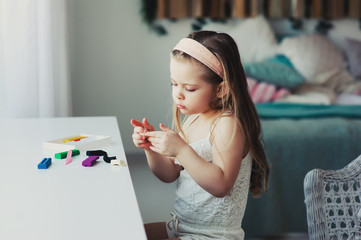 cute toddler girl playing with plasticine or play dough at home. Child learning to work with modelling clay