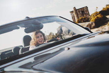 Happy girl with curly hair drives a cabriolet over a mountain serpentine on a summer sunny day