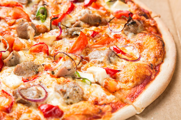 Tasty pizza close up in a box. Pizza with onion, tomatoes, cheese, meat and pepper. Selective focus