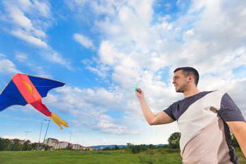 Portrait of happy young man with flying kite on a meadow