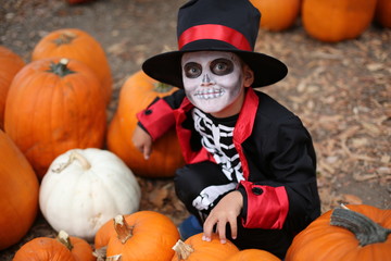 Trick or treat. Boy in a Halloween costume of skeleton sits between orange pumpkins on a Pumpkin patch
