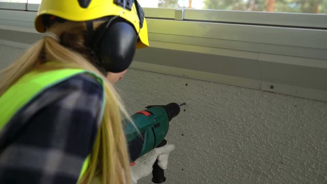 Young Female construction worker drilling concrete wall with the drill and smiling at the camera.