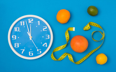 Time to diet concept: Clock, grapefruit, orange, lemon, lime and measuring tape on blue background....