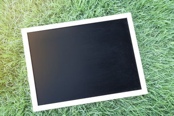Blank black chalkboard on grass.