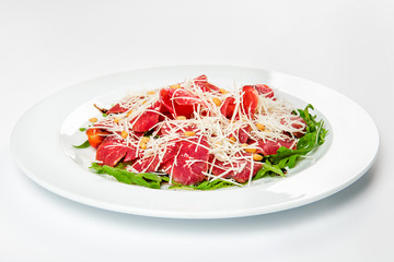 Meat platter with cheese, corn, tomatoes and arugula on plate.