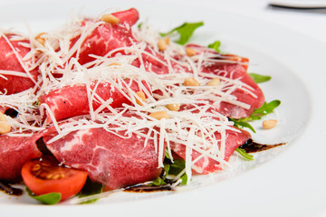 Meat platter with cheese, corn, tomatoes and arugula on plate.
